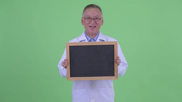 Happy Mature Japanese Man Doctor Talking While Holding Blackboard