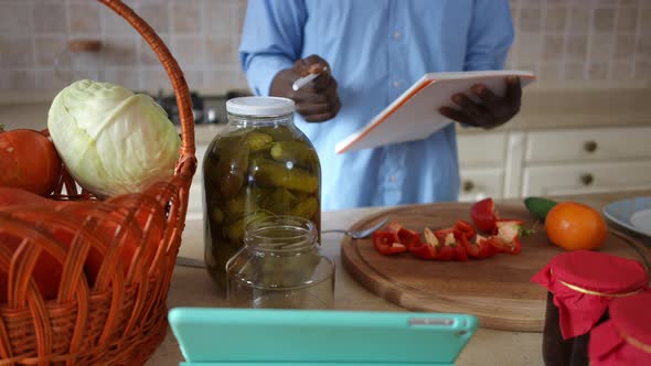 Unrecognizable African American Young Man Writing Recipe Canning Vegetables in Kitchen at Home