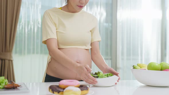 Asian young pregnant woman choose to eat green salad instead of donut.