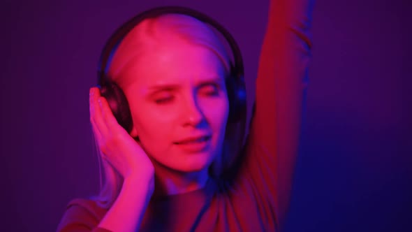 Stylish Woman Listening Music in Headphones and Dancing Energetic and Rhythm in Pink and Blue Light