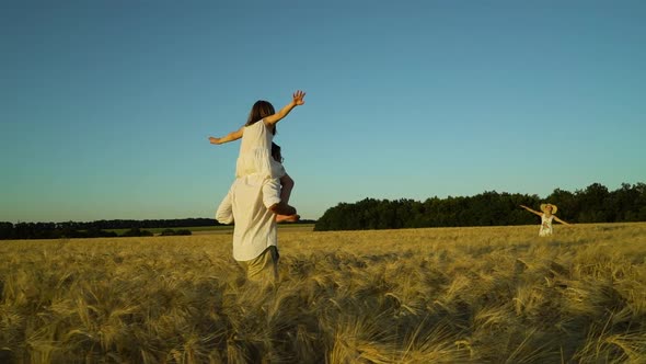 Girl Sitting on Shoulders of Father Walking in Field