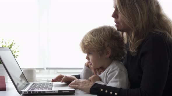 Woman with little kid working on laptop at home