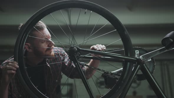 A Male Cyclist in a Plaid Shirt Repairs a Bicycle in a Garage Turns a Wheel and Checks It