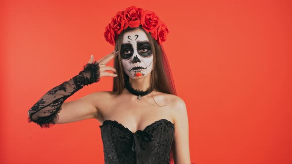 Day of Dead Woman with Sugar Skull Makeup Acting Like Shooting Herself While Posing Against Red