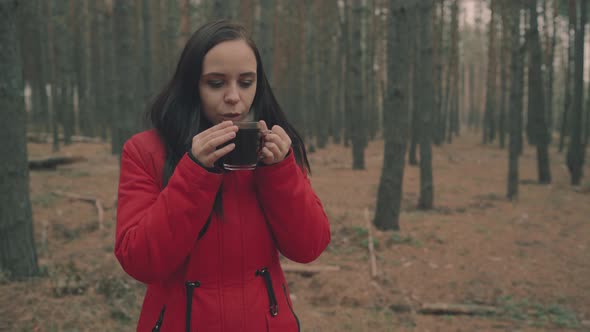 A Pretty Young Woman in Casual Clothes is Drinking a Tea to Keep Warm in a Cold Weather in Woods