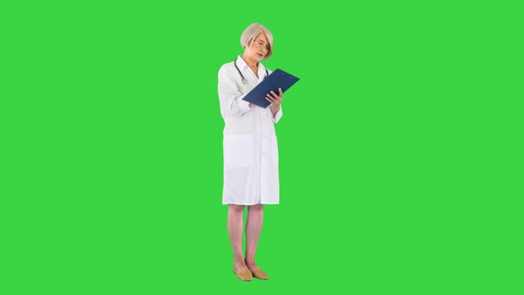 Serious Mature Doctor Woman Writing in Clipboard on a Green Screen Chroma Key