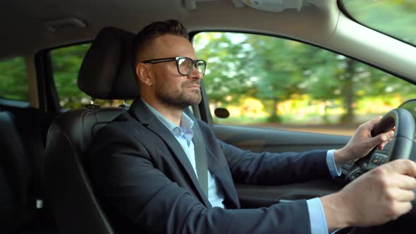 Formally Dressed Bearded Man in Glasses Driving a Car in Sunny Weather