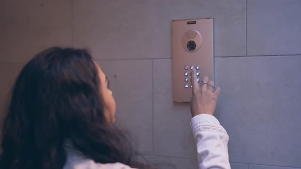 Young Spanish Girl Presses Buttons On Numeric Keypad Of Video Intercom Installed On Tiled Interior