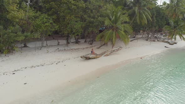 Aerial: woman relaxing on white sand beach turquoise water tropical Indonesia