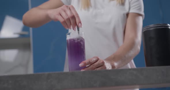 Female Hand Stirs Colored Bsaa of Purple Color Into Glass of Water