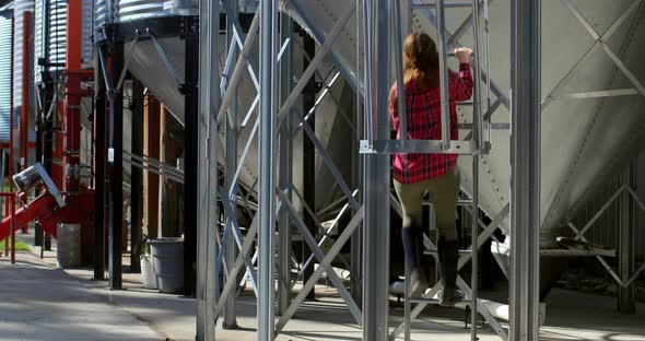 Rear view of caucasian female worker climbing ladder by storage tank 4k