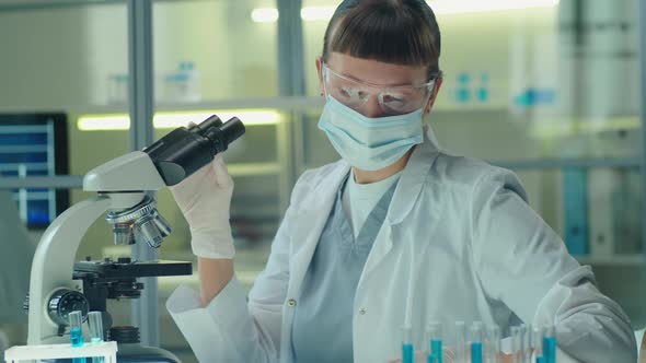 Female Scientist in Mask and Glasses Working with Microscope in Lab