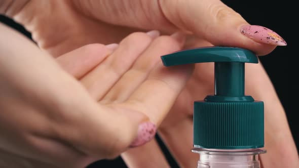 Woman Pushes Dispenser and Liquid Soap Flows Into Her Hand on Black Background