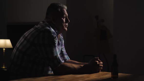 Upset Senior Man Is Alone with Bottle of Beer in Dark Room