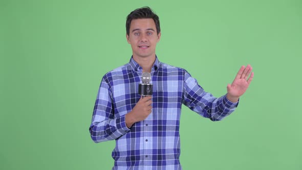 Happy Young Handsome Hipster Man Presenting Something with Microphone