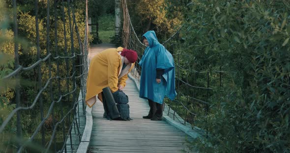 Man and Woman Hikers Walking on Bridge Over River Drinking From Vacuum Flask