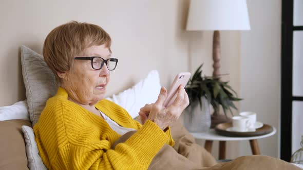 Grandmother Using Mobile Phone Resting At Home In Bed