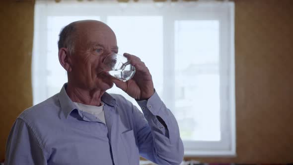 Portrait of Attractive Old Man Quenching Thirst Drinks Cool Clear Water From Glass Beaker Smiling