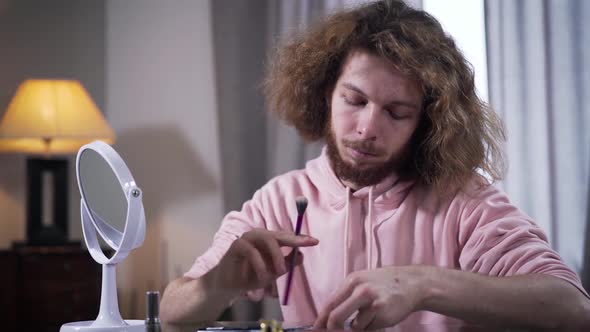 Close-up Portrait of Caucasian Binary Gender Person Applying Face Powder and Looking at Mirror