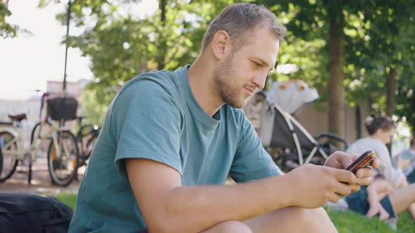 Bearded Man Scrolling News Looks at Smartphone Smiling