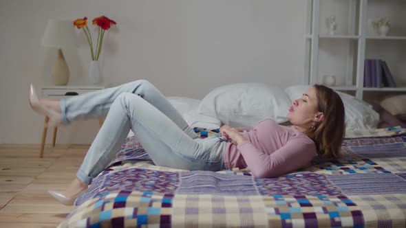 Upset Pretty Woman Lying on Bed Struggling to Fit Into Tight Jeans After Gaining Weight Indoors