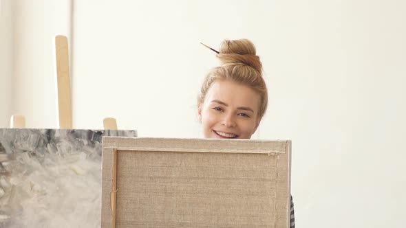 Portrait of Charming Girl Artist Smiling Flirtatiously and Covering Her Face with Her New Painting