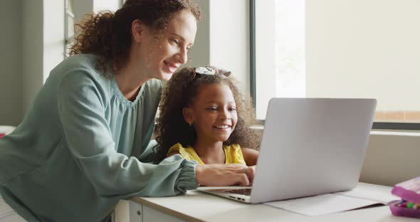 Video of happy caucasian female teacher explaining lesson on laptop to african american girl