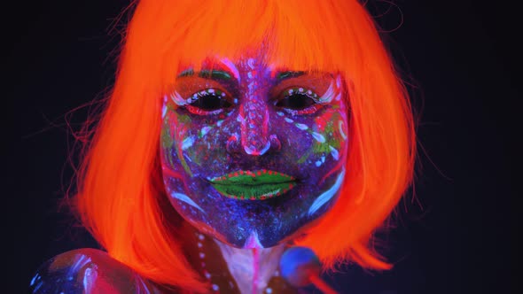 Girl with UV Drawings on Her Body with a Lollipop in Neon Light in the Dark