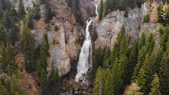 Flying over a green forest around a big waterfall in the mountains. Waterfall Aerial View.