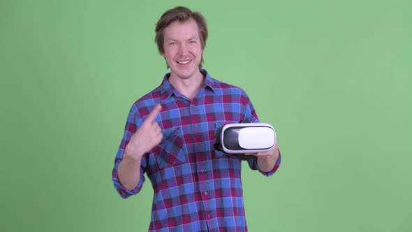 Happy Young Hipster Man Holding and Pointing at Virtual Reality Headset