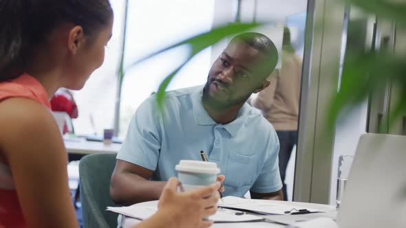 Diverse male and female business colleagues talking and taking notes in office