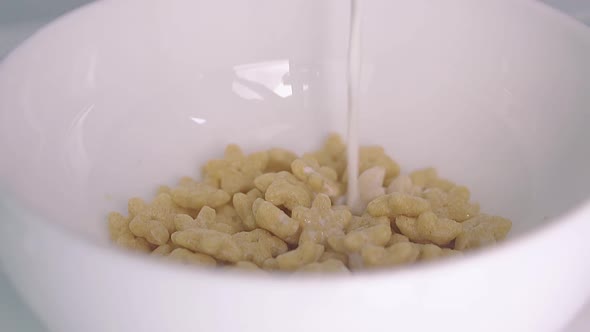 Man Pours Milk Into White Bowl with Delicious Honey Cereals