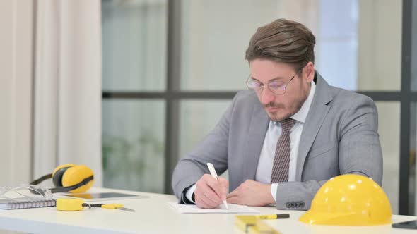 Middle Aged Engineer Writing on Paper in Office