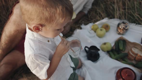 A Little Boy Drinks Milk From a Glass Through a Straw While Sitting in a Family Circle at a Picnic