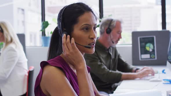 Portrait of mixed race businesswoman sitting using computer talking on phone headset in office