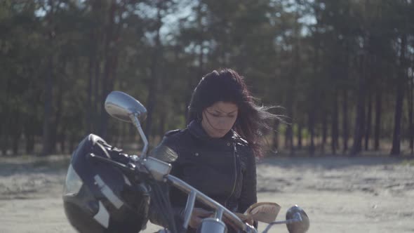 Back View of the Pretty Caucasian Girl in a Black Leather Jacket Sitting on the Motorcycle Reading