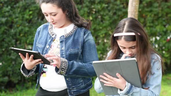 Two Young Girls Relaxing Outdoor Playing with Tablet