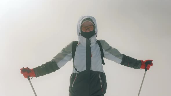 A Young Woman is Standing on Top of a Mountain and Looking at the Camera