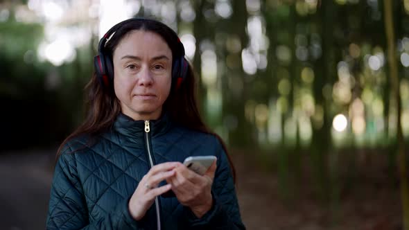 Portrait of a Pretty Adult Woman with Wireless Headphones Standing in a Park and Listening to Music