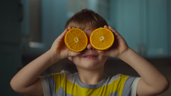 Preschooler boy holding two halves of orange fruit in hands, taking it to eyes