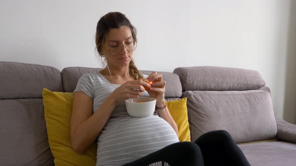 Beautiful pregnant woman with glasses peals tangerine and eats it