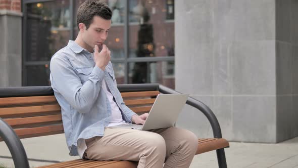 Pensive Young Man working on Laptop, Sitting on Bench
