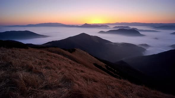 Sunrise in a mountain landscape. Low inverse clouds in the valley between the hills.
