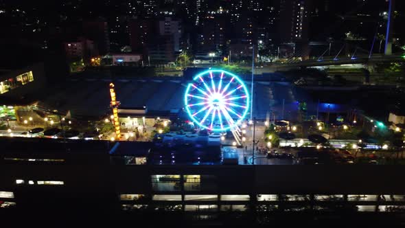 Side aerial view of an amusement park at night with lights and people enjoying