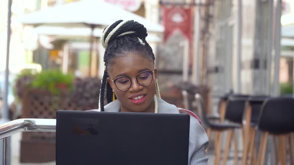 African American Woman in Street Cafe Works on Her Laptop