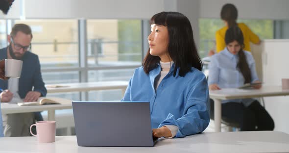 Beautiful Asian Woman Freelancer Working on Laptop with Coffee Cup in Office