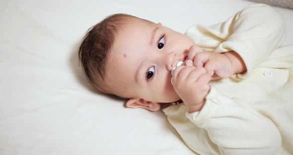 Newborn Cheerful Littlebaby is Chewing and Playing in His Crib with Nipple