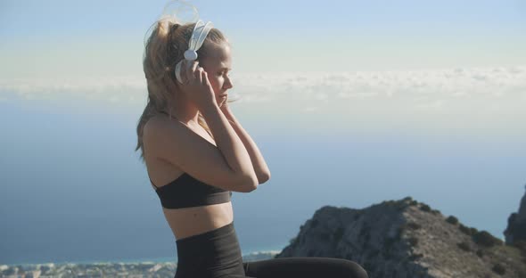 Young Woman Putting On Headphones On Mountaintop