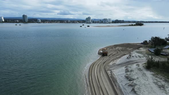 Highing drone view following a large dump truck carrying sand along a coastal beach road.