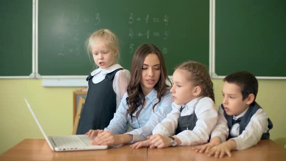 Children and Teacher Discussing and Looking at Laptop in the Classroom alt